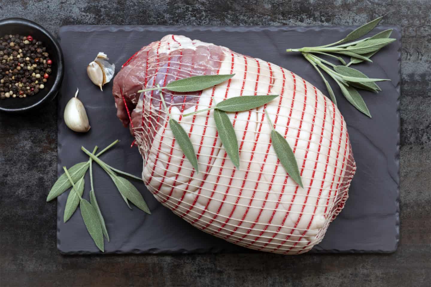 Raw pork roast, top view on slate, with sage leaves, garlic and black peppercorns